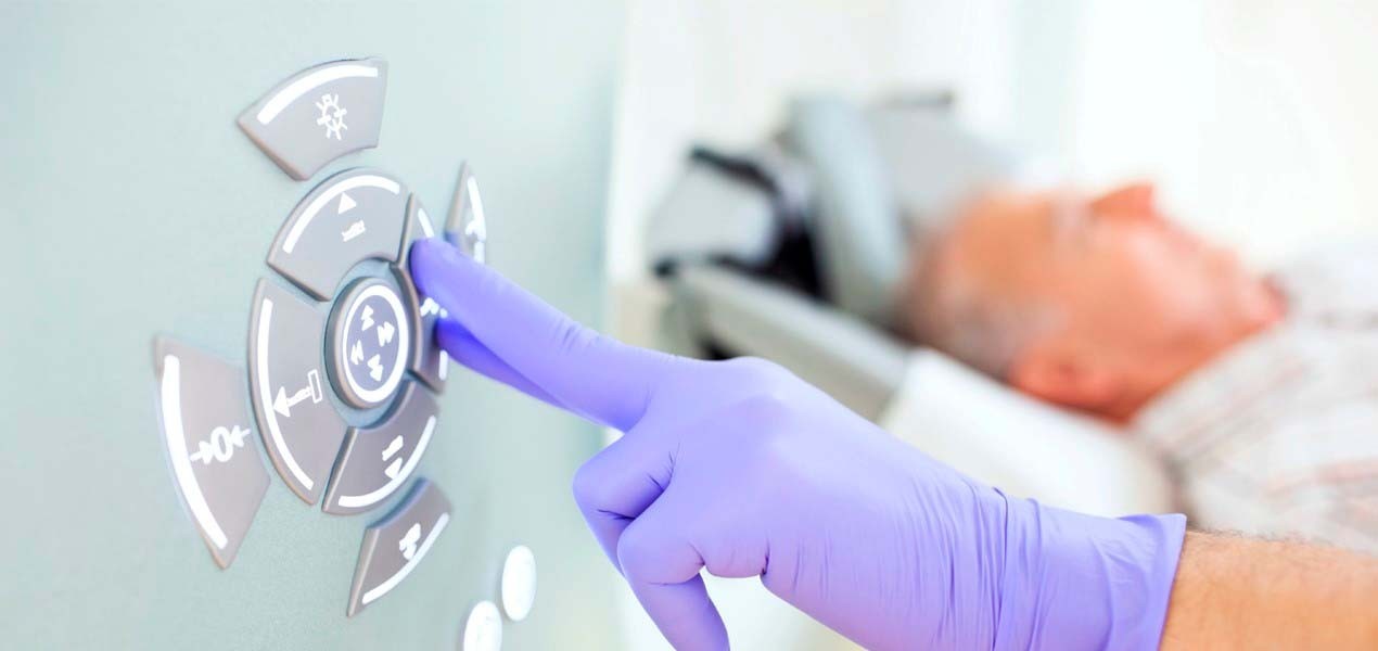 Kuvituskuva: Lääkärin käsi kumihanskassa painaa magneettikuvauslaitteen nappia.